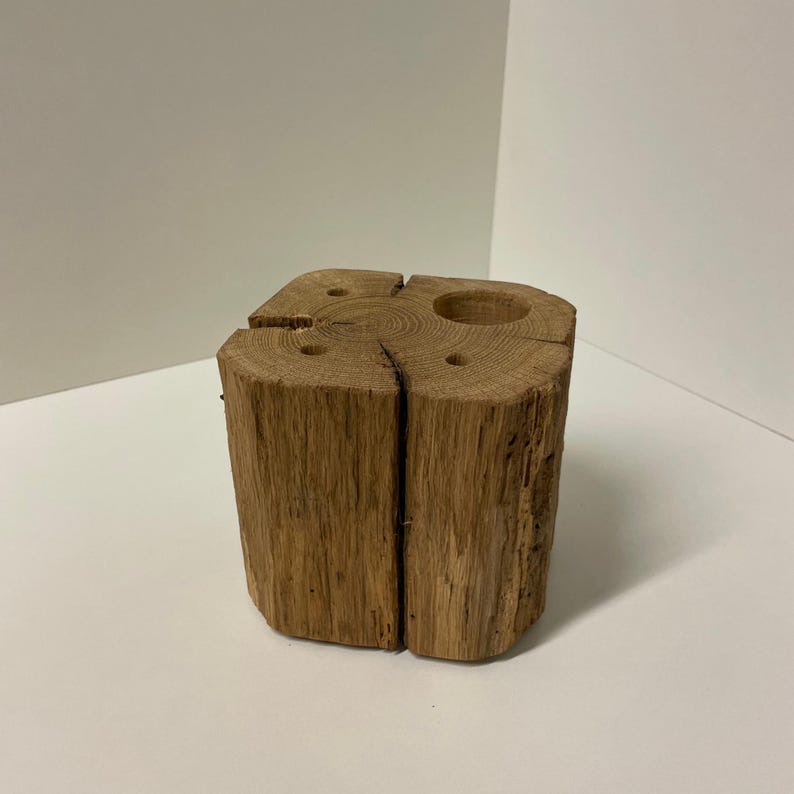 May include: A rustic, square wooden candle holder with a natural, light brown finish. The holder features a large circular opening and several smaller holes for candles. The wood grain is visible, adding to its natural aesthetic. The candle holder is a decorative item.