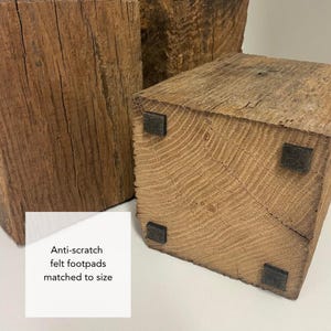 May include: Two rectangular blocks of weathered brown wood with visible grain and texture. The base of the foreground block features four small, square, black anti-scratch felt footpads. A white label with the text Anti-scratch felt footpads matched to size.