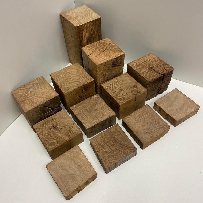 May include: A collection of twelve natural wood blocks of varying heights and thicknesses, featuring visible grain patterns, knots, and cracks. The blocks are arranged in a tiered formation, showcasing the raw, textured surfaces of the light brown wood.