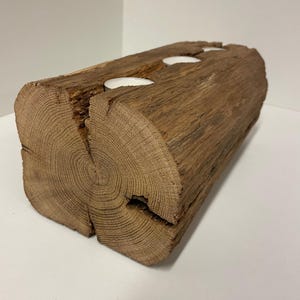 May include: A rustic, brown wooden candle holder with two circular openings for tea light candles. The candle holder is made from a section of a log, showcasing the natural wood grain and texture. The tea lights are white.