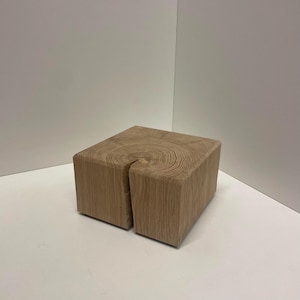 Könnte beinhalten: Ein quadratischer Block aus hellem Naturholz mit sichtbarer Maserung auf der Oberseite. Der Holzblock weist einen deutlichen vertikalen Riss auf, der sich von der Mitte der Oberkante über eine Seite des würfelförmigen Objekts nach unten erstreckt.