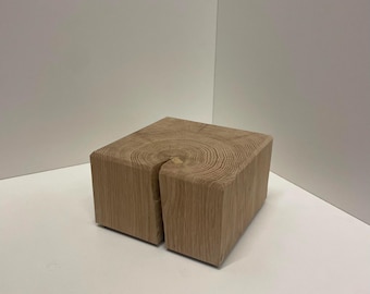 Könnte beinhalten: Ein quadratischer Block aus hellem Naturholz mit sichtbarer Maserung auf der Oberseite. Der Holzblock weist einen deutlichen vertikalen Riss auf, der sich von der Mitte der Oberkante über eine Seite des würfelförmigen Objekts nach unten erstreckt.