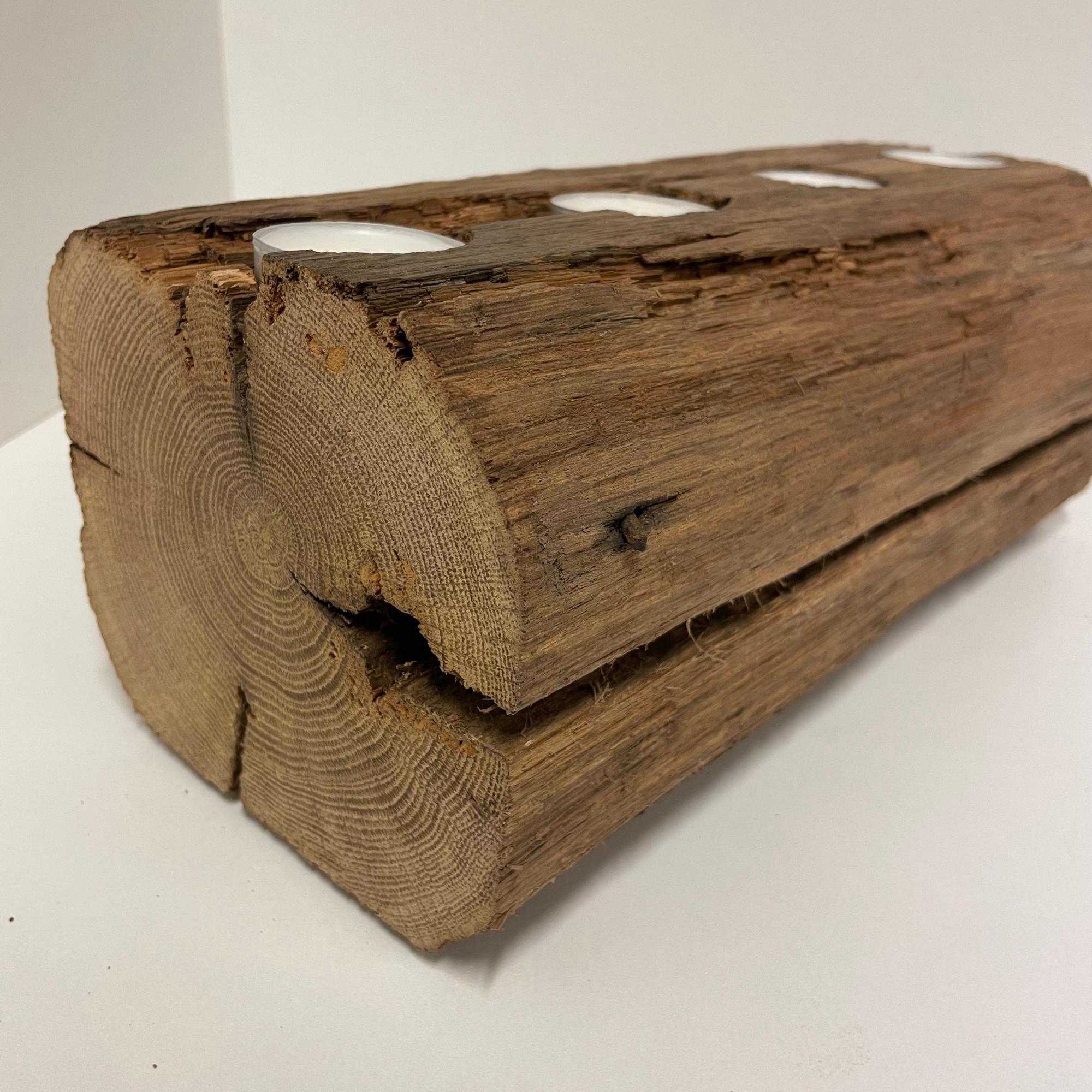 May include: A rustic wooden candle holder made from a section of a log. The brown log has four circular cutouts holding white tea light candles. The wood grain and natural imperfections are visible, adding to its charm.