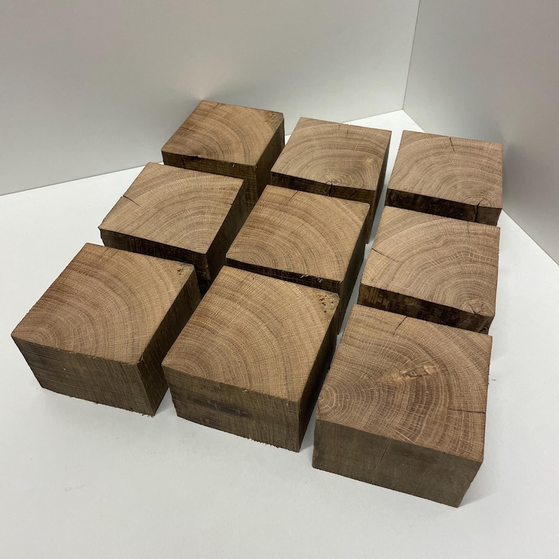 May include: A collection of nine square wooden blocks arranged in a three-by-three grid. Each block features a natural light brown wood grain pattern with visible growth rings on the top surface and a smooth, unfinished texture on the sides.