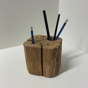 May include: A rustic wooden pencil holder with a natural, split-log design. The holder contains four pencils: two blue and two black. The wood has a warm, brown tone, and the pencil holder is a unique desk accessory.