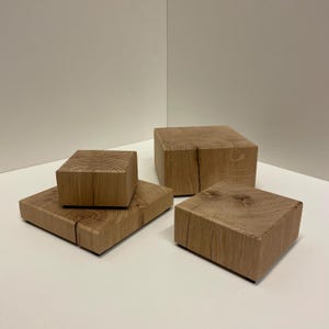 Puede incluir: Un conjunto de cuatro bloques de madera de color marrón claro de diversas alturas y tamaños, cada uno con un patrón de veta de madera natural visible y una grieta vertical distinta que atraviesa el centro de las superficies cuadradas.