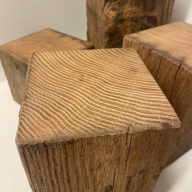 May include: A collection of four square wooden blocks made from reclaimed timber. Each block features a distinct, weathered brown surface with visible grain patterns and natural textures on the top and sides, showcasing the raw, organic wood.