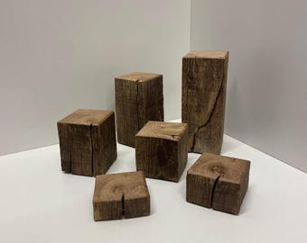 Könnte beinhalten: Eine Ansammlung von sechs naturbraunen Holzblöcken in unterschiedlichen Höhen und Breiten. Jeder Block weist eine sichtbare Holzmaserung und einen deutlichen vertikalen Riss auf, der durch die Mitte der Oberseite verläuft und die raue Textur zeigt.