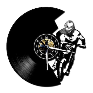 Puede incluir: Reloj de vinilo negro con la silueta de un piloto de motocross. La esfera del reloj es visible con números y manecillas blancas, y el piloto está en movimiento. Las manecillas del reloj indican la hora.