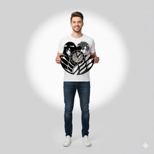Può includere: Un orologio da parete a tema anime in bianco e nero. L'orologio presenta due personaggi anime e un quadrante con numeri. L'orologio è tenuto da una persona che indossa una maglietta bianca e jeans blu.