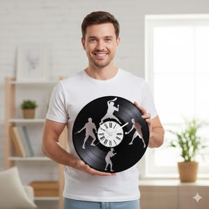 Könnte beinhalten: Eine schwarze Vinyl-Schallplattenuhr mit silbernen Silhouetten von Badmintonspielern um ein weißes Zifferblatt mit römischen Ziffern. Die Uhr wird von einer Person gehalten, die ein weißes T-Shirt trägt.