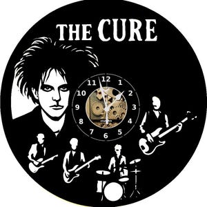 Könnte beinhalten: Schwarze Vinyl-Schallplattenuhr mit der Band "The Cure". Das Zifferblatt hat ein Zahnraddesign in der Mitte. Die Bandmitglieder sind weiß silhouettiert. Der Text "THE CURE" steht oben.