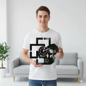 Puede incluir: Reloj de vinilo negro con la silueta de un miembro de la banda y el logotipo. El reloj tiene una esfera negra con números blancos y manecillas rojas. El reloj lo sostiene una persona que lleva una camiseta blanca.