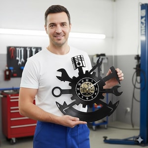 Könnte beinhalten: Eine schwarze Wanduhr in Zahnradform, die Werkzeuge wie Schraubenschlüssel und einen Kolben integriert. Das Zifferblatt zeigt Zahnräder und Zeiger. Die Uhr wird von einer Person gehalten, die ein weißes T-Shirt und blaue Latzhosen trägt.