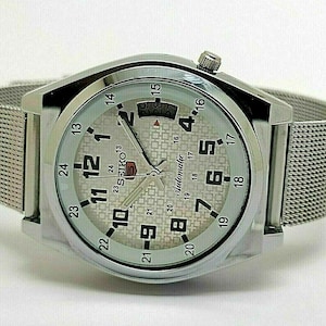 May include: Silver Seiko automatic wristwatch with a mesh strap. The watch face is light grey with black numerals and hands. The watch has a date display and the word "automatic" is printed on the face.