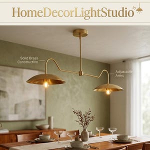 May include: A brass-coloured, two-light pendant light fixture with adjustable arms and solid brass construction. The fixture is suspended from the ceiling and has two lampshades. The text "HomeDecorLightStudio" is at the top.