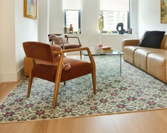 May include: A living room scene featuring a light brown leather sofa, two brown armchairs, and a patterned rug with floral motifs. The room has large windows with white blinds and hardwood flooring.