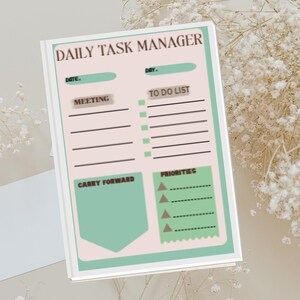 May include: A Daily Task Manager notepad with a white border, featuring a pastel color scheme. The notepad includes sections for date, day, meetings, to-do lists, carry forward items, and priorities. The text "Daily Task Manager" is at the top.