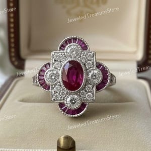 May include: A silver ring featuring an oval ruby centre stone, encircled by smaller rubies and diamonds. The ring, in an Art Deco design, is presented in a wooden jewellery box.