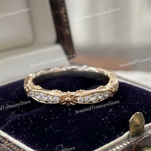 Peut inclure: Une bague dorée ornée d'un motif floral et de petits pierres précieuses transparentes. La bague est présentée sur un fond de velours bleu foncé à l'intérieur d'un écrin marron. Le texte "Jeweled Treasure Store" est visible.