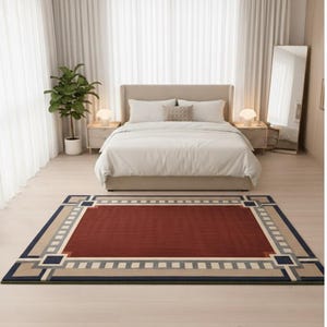 Peut inclure: Tapis rectangulaire à motifs géométriques dans une chambre. Le tapis présente un champ central bordeaux, bordé de motifs géométriques beiges, gris et bleu marine. La pièce comprend un lit, des tables de chevet et un miroir pleine longueur. Dimensions: 200cm x 300cm.