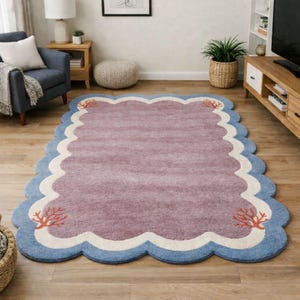 May include: A rectangular rug with a scalloped edge design. The rug features a mauve center, a white border, and a light blue scalloped edge. Coral reef designs are placed on the corners. The rug is placed on a hardwood floor.