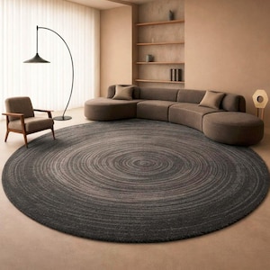 May include: A circular grey rug with a spiral pattern is the focal point of a contemporary living room. The rug is surrounded by a brown sofa, a wooden armchair, and a black floor lamp. The room has a neutral colour palette and a curved sofa.