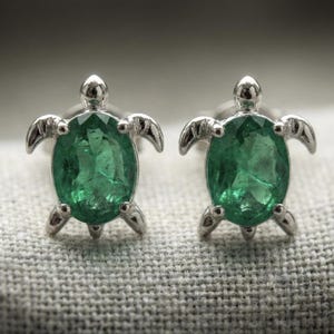 May include: A pair of sterling silver turtle stud earrings. Each earring features a vibrant green oval-cut gemstone set within a turtle-shaped frame. The turtles have detailed flippers and heads, creating a charming and whimsical design.