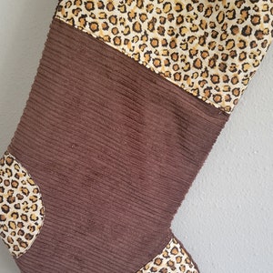 May include: A brown corduroy Christmas stocking with a leopard print cuff and toe.