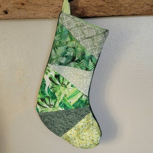 May include: A green Christmas stocking with a patchwork design featuring various green and white patterns, including ferns, leaves, and polka dots.