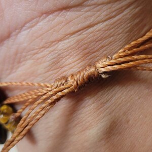 May include: A brown and gold tiger's eye stone bracelet with a brown cord tie closure.