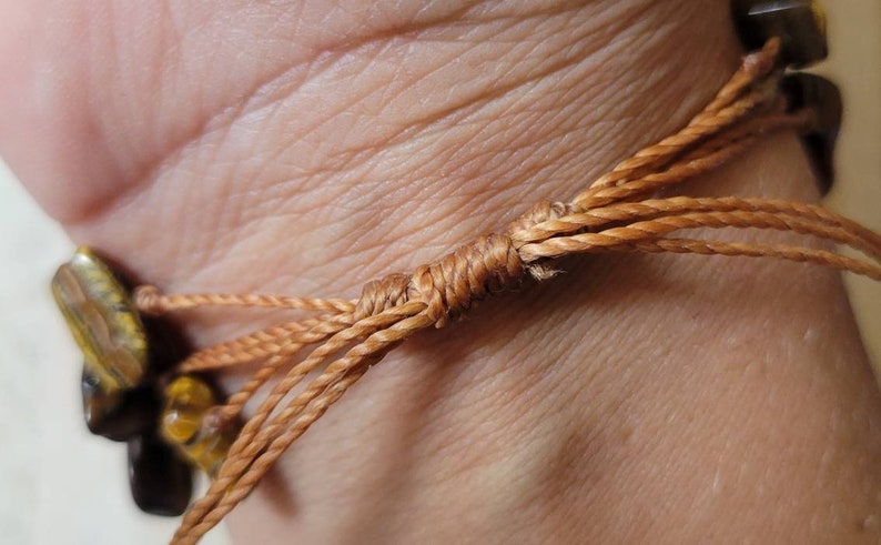 May include: A brown and gold tiger's eye stone bracelet with a brown cord tie closure.