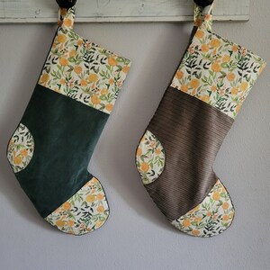 May include: Two Christmas stockings with a floral pattern in shades of yellow and green. One stocking is green corduroy with a yellow floral cuff, and the other is brown corduroy with a yellow floral cuff.
