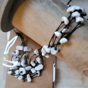 May include: A multi-strand bracelet with white stones and black cord. The bracelet is wrapped around a wooden spool.