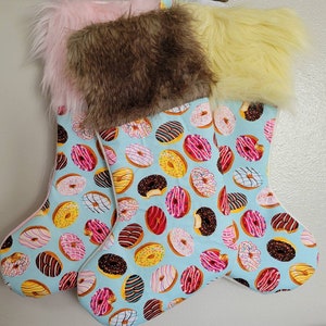 May include: A pair of blue Christmas stockings with a donut pattern. The stockings are trimmed with pink and yellow faux fur.