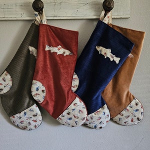 Może przedstawiać: Cztery świąteczne skarpety z sztruksu w odcieniach brązu, czerwieni, granatu i beżu, każda ozdobiona aplikacją w kształcie ryby. Palec i mankiet mają wzorzystą tkaninę z przynętami wędkarskimi.