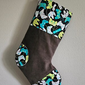 May include: A brown and black Christmas stocking with a green, white, and yellow pattern of video game controllers.