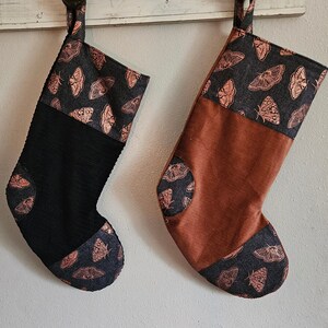 May include: Two Christmas stockings with a brown and black corduroy fabric and a copper butterfly print. One stocking is black with a brown cuff and the other is brown with a black cuff.