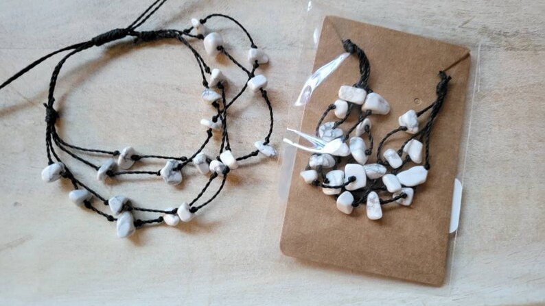 May include: A set of two necklaces with white stone beads and black string. The necklaces are layered and have a simple design.