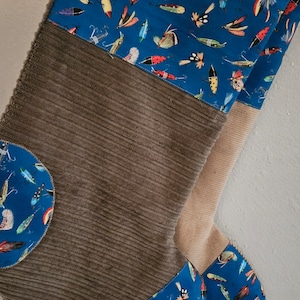 Peut inclure: Une chaussette en velours côtelé marron avec du tissu bleu en haut et en bas. Le tissu bleu a un motif de leurres de pêche colorés.