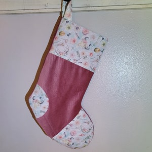 May include: A pink and white Christmas stocking with a floral pattern and a corduroy fabric panel. The stocking has a loop at the top for hanging.
