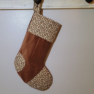 May include: A brown and tan Christmas stocking with a gingerbread man pattern. The stocking is made of corduroy and fabric and has a loop at the top for hanging.