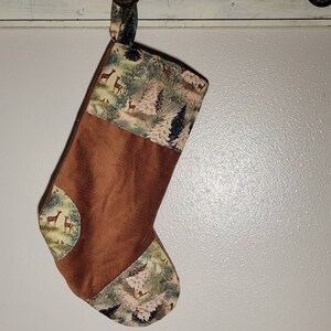 May include: A handmade Christmas stocking with a brown corduroy body and a forest-themed fabric top and accents. The fabric features deer, trees, and foliage in shades of green, brown, and cream. A loop is attached for hanging.