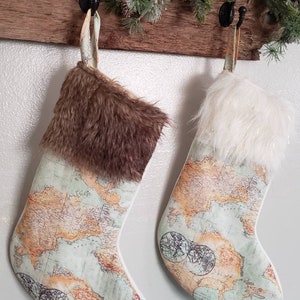 Op de afbeelding: Twee kerstsokken met een wereldkaartontwerp. Eén sok heeft een bruine nep bontmanchet en de andere heeft een witte nep bontmanchet.