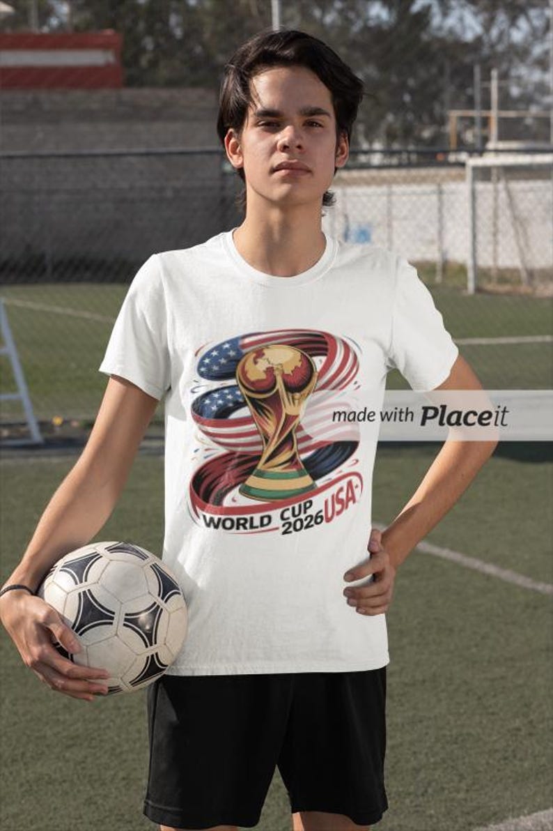 May include: White t-shirt featuring a graphic of the World Cup trophy with the American flag and the text "World Cup 2026 USA". The person is holding a soccer ball.