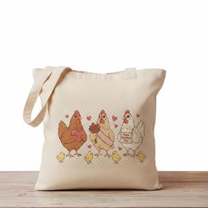 May include: Cream-colored tote bag featuring a whimsical illustration of three chickens with hearts and chicks. One chicken holds a heart, another a bouquet, and the third a sign that reads "Happy Valentine's Day".
