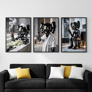 May include: Set of three framed art prints featuring a black figure with yellow cross-eyes in various bathroom scenes. One print shows the figure in a bathtub with money, another holding a bottle, and the last one sitting on a toilet, all smoking cigars.