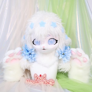 May include: A white furry doll head with blue star accents and large blue eyes. The doll has blue flower accents and white furry paws with pink pads. The text "FDW Handmade" is visible on a red and white tag.