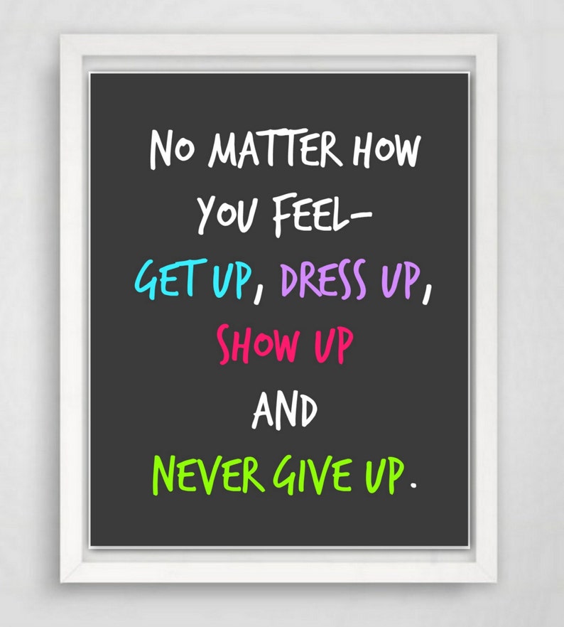 May include: A framed print with a black background and white text that reads "NO MATTER HOW YOU FEEL - GET UP, DRESS UP, SHOW UP AND NEVER GIVE UP." The words "GET UP", "DRESS UP", "SHOW UP", and "NEVER GIVE UP" are in blue, purple, pink, and green.