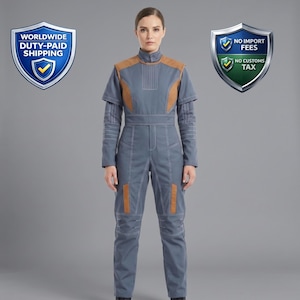 Peut inclure: Combinaison grise avec des détails marron et des coutures blanches. La combinaison a un col montant, des manches courtes et des rembourrages sur les épaules et les genoux. Le modèle est devant un fond gris.